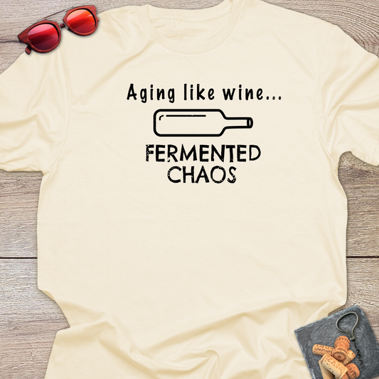 A cream-coloured t-shirt with a black graphic that reads 'Aging like wine. Fermented Chaos.' And a graphic of wine bottle in between the two statements.