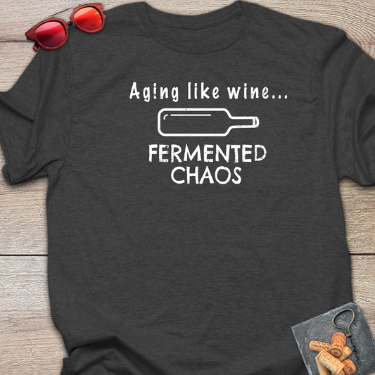 A dark heather gray t-shirt with a white graphic print that reads 'Aging like wine. Fermented Chaos.' And a graphic of wine bottle in between the two statements.
