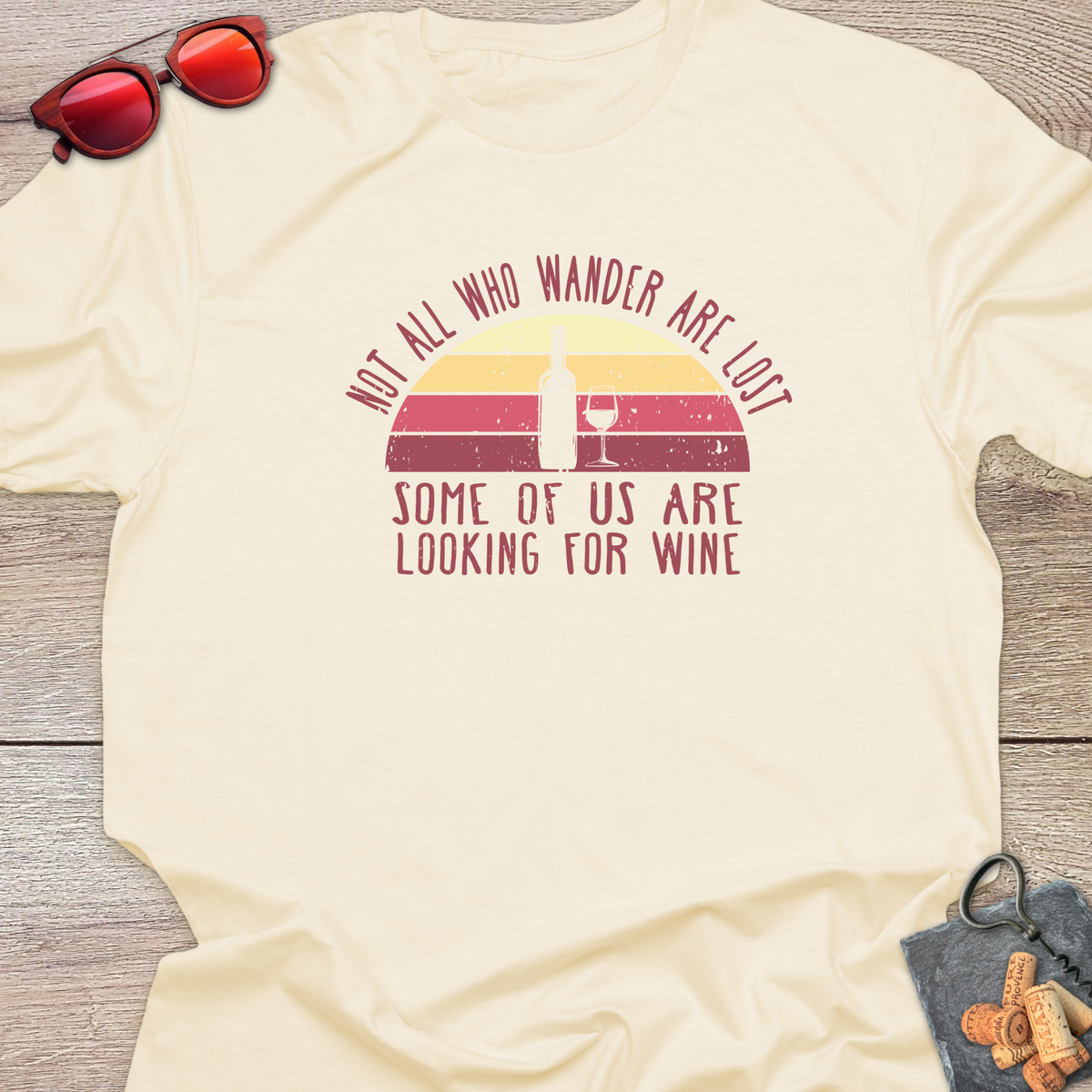 A natural colour t-shirt with a retro sunset design and the saying "Not all who wander are lost...some of us are looking for wine". 